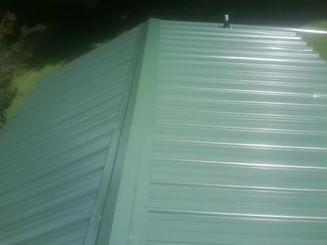 New green metal panels meeting at the ridge of a roof — Flat Roof Repair work by our crew in New Castle