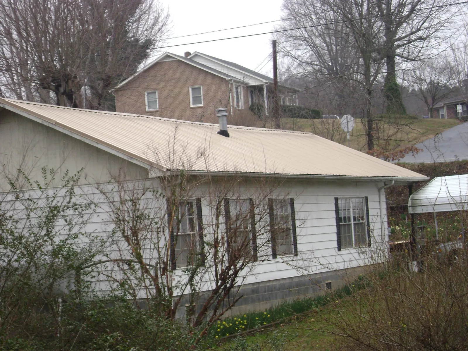 Tan metal roof on a white sided house set into a hillside — Commercial Roofing by Roofing Brothers in New Castle