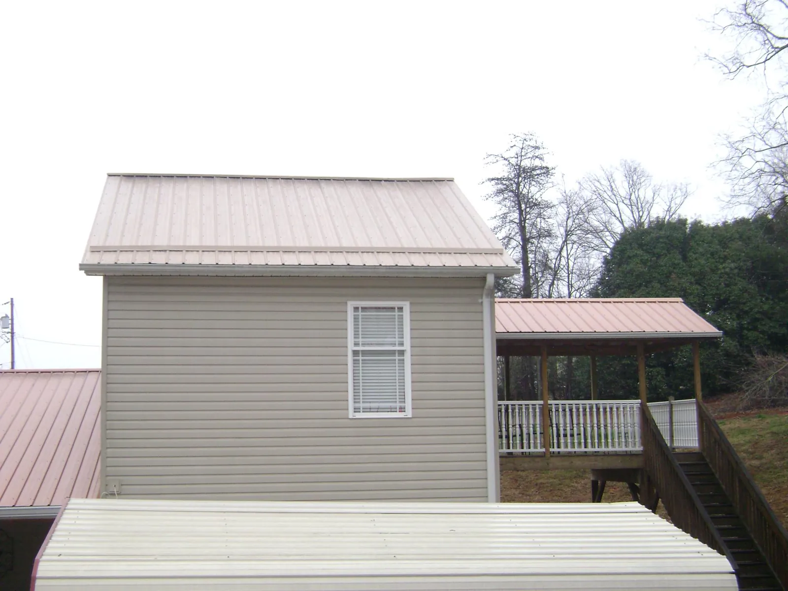 Tan metal roofs on a two story addition and attached porch, from a Roof Replacement job in New Castle